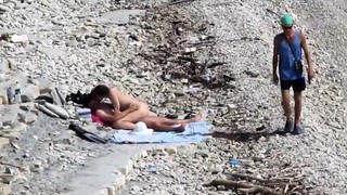 Couple having sex on a nudist beach while people pass by